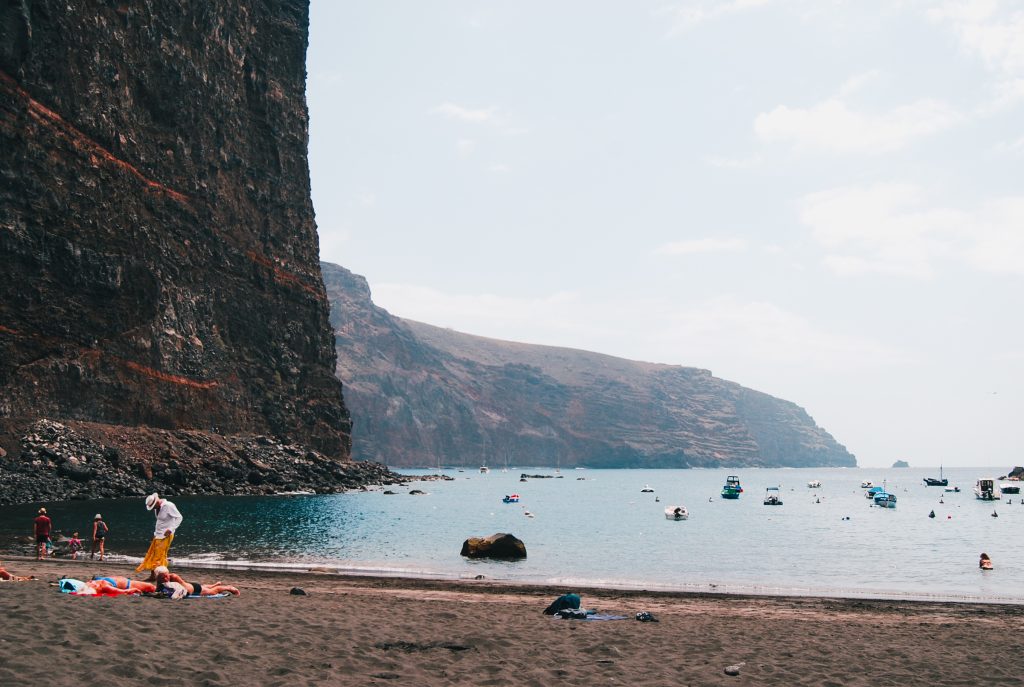 Sandy beach next to a mountain, people are bathing in the ocean.